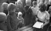 Inskrivning barngymnastik 15 september 1965

Barnen som ska skrivas in samlas runt lärarinnan, Inga Pettersson, tillsammans med några föräldrar. Ett barn fnissar. I mitten ett litet barn i 1-2 år med en stickad så kallad hjälmmössa.