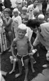 Simpromotion, 20 augusti 1965

Simskoleavslutning, barn och föräldrar i kö. Pojken i förgrunden håller korkdynor i händerna