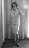 Modebilder 23 april 1966

Närbild på en mannekäng i vit dräkt med kort kjol och svarta lågklackade skor med remmar på. Hon har ett pärlhalsband om halsen och håller upp sin vänstra hand i en pose i riktning mot halsen. Hon bär glasögon.