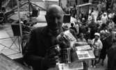 Göingeflickorna 4 september 1965

På bilden i förgrunden är det en man som håller i sina händer förpackningar med 'Wasa spisbröd', 'Kellogg's Corn Flakes', 'Pilsner korv', 'Luxus kaffe' osv. På bilden i bakgrunden syns en karusell och människor ute i stadsmiljö.