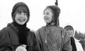 Hästnäs,  20 januari 1966

I bildens förgrund syns det två flickor och en flicka syns det i bakgrunden åt höger. Alla flickor på bilden har stickade vintermössor på sina huvuden. På sina halsar har de två flickorna långa stickade skarfar som når till deras knän. En flicka i mitten är klädd i en anorakliknande jacka.