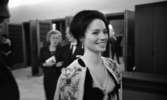 Premiär Julie, 28 februari 1966

Finklädd dam i teaterns foajé. Hon är klödd i klänning med broderad kofta, pärlhalsband samt örhängen. Andra personer skymtar i bakgrunden.