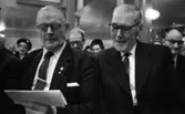 Pensionärspop 2 mars 1966

I förgrunden på bilden syns det två herrar som sitter bredvid varandra. Båda bär glasögon och är klädda i mörka kostymer, ljusa skjortor med mörk slips. Herren som sitter till vänster på bilden håller i sin vänstra hand ett sånghäfte. Han sjunger. I bakgrunden på bilden skymtar det andra herrar och damer. Damerna på bilden bär glasögon och har hattar på sig.