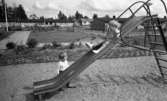 Lekplatserna tråkiga 7 juli 1965

Två små barn leker på lekplatsen. Det ena barnet åker rutschkana. Det andra barnet står bredvid rutschkanan.