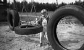Lekplatserna tråkiga 7 juli 1965

En liten flicka på lekplats i bostadsområde. Hon står vid en gunga och håller sin lilla docka i ena handen.