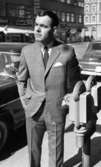 Andersson Gustavsson mode 23 april 1966

En manlig fotomodell visar herrkläder. Han är iklädd kostym, skjorta och slips. Han står utomhus på en gata och håller sin vänstra hand på en parkeringsautomat. Bilar och hus syns i bakgrunden.