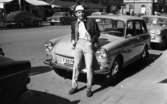 Andersson Gustavsson mode 23 april 1966

En manlig fotomodell visar herrkläder. Han är iklädd jacka, tröja. byxor, skor, handskar och hatt. Han lutar sig mot motorhuven på en parkerad bil. I bakgrunden syns flera bilar samt personer och hus.