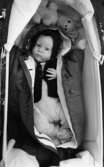 Babykläder, 6 april 1966

En baby ligger i en barnvagn och tittar. Den är iklädd sparkdräkt, jacka och mössa. Vid huvudänden lligger ett gosedjur.










































































































or. Han går nedför en kort trappa utomhus.