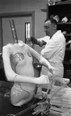 Ortopeden 28 februari 1966

Herr Holmgren i vit rock visar funktionen hos en armprotes. Framför honom på bordet står en gipskropp för utprovning av hjälpmedel till fysiskt handikappade. I förgrunden ligger diverse ortopedverktyg. I bakgrunden syns hyllor fyllda med proteser.