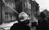 Noraskola brinner 18 februari 1966

Det brinner i en skola i Nora en vinterdag. I bildens förgrund syns en brandman samt en civilklädd man som samtalar. I bakgrunden syns ytterligare en brandman som har riktat en brandsprutas vattenstråle mot husfasaden.