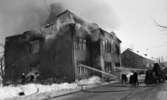Noraskola brinner 18 februari 1966

Det brinner i en skola i Nora en vinterdag. Uniformerade brandmän och en civilkläd man syns på bilden. Brandmän riktar brandsprutors vattenstrålar mot skolbyggnadens fasad. Det syns rökutveckling på skoltaket.
