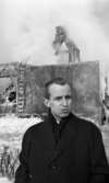 Nora-branden efteråt, 19 februari 1966

I förgrunden syns det en man som är klädd i en mörk rock. I bakgrunden skymtar det som är kvar av byggnaden efter brand. Istappar hänger på byggnaden.