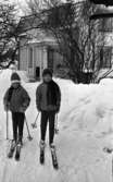 Orubricerat 8 januari 1966

Två barn på skidor poserar framför ett trähus med trädgård