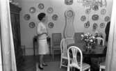 Hemma hos Ignell 8 januari 1966

Porträtt av medelålders kvinna i matsal med antika matsalsmöbler, i bakgrunden en stående klocka av modell Moraklocka, till vänster ett större barockliknande skåp, mängder av porslinsfat dekorerar väggen, i taket skymtar en kristallkrona