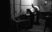 Hattfabrik läggs ned 1 mars 1966

Två arbetare med bara överkroppar tvättar sig i ett tvättställ inne på ett hattmakeri.