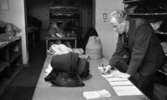 Hattfabrik läggs ned 1 mars 1966

Man i mörk kostym står vid ett skrivbord och skriver på papperslappar. Framför honom ligger hattar som han betraktar.