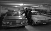 Bilhall 30 mars 1966

Två män står i ett garage och tittar på en bil. En av männen bär kostym. Den andre mannen bär arbetskläder. Andra bilar syns i bakgrunden.