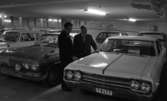 Bilhall 30 mars 1966

Två män står i ett garage och tittar på en bil. En av männen bär kostym. Den andre mannen bär arbetskläder. Andra bilar syns i bakgrunden.