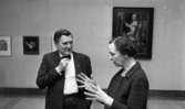 Nationalmuseum 1 31 maj 1966

En man och en kvinna står inne på länsmuseet och diskuterar. Mannen är klädd i svart kostym, svart fluga och vit skjorta. Kvinnan är klädd i en svart dräkt med knappar på. Tavlor hänger på väggen i bakgrunden.