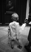 Barn på konstutställning 12 april 1966

En liten flicka klädd i en klänning med volang står mitt på golvet i en konstutställningslokal. I vänstra handen har hon en sele.






















































































































or. Han går nedför en kort trappa utomhus.