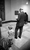 Barn på konstutställning 12 april 1966

En liten flicka klädd i klänning med volang och knappar i ryggen står bredvid en kostymklädd man inne i en konstutställningslokal. En bonad och en tavla hänger på väggen. Till höger i bakgrunden syns en dam klädd i kappa och hatt.






















































































































or. Han går nedför en kort trappa utomhus.