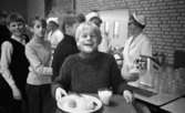 Barnbespisning 1 april 1966

I förgrunden står en ung pojke med en bricka i sina händer. Han skrattar. På brickan står ett fat med mat, ett glas mjölk och bestick. I bakgrunden syns en kö av barn. Någon tappar upp mjölk i ett glas ur en behållare. Bakom disken står tre damer som serverar barnen mat. De är klädda i vita arbetsuniformer med vita hattar på sina huvuden.



























































































































or. Han går nedför en kort trappa utomhus.