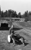 Hundarna i Mosås 4 maj 1966

I förgrunden står en stor schäfer framför en kvinna som sitter på en tunna. I bakgrunden syns en trakor samt hus.




























































































































































































































































































or. Han går nedför en kort trappa utomhus.