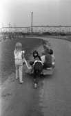 Oläslig rubrik 23 augusti 1965
 
Fyra barn sitter på en bräda med hjul under och tre andra drar och skjutsar på. De befinner sig vid ett bostadsområde.
