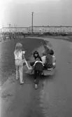 Oläslig rubrik 23 augusti 1965
 
Fyra barn sitter på en bräda med hjul under och tre andra drar och skjutsar på. De befinner sig vid ett bostadsområde.