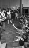 Popgala i Kumla, Farlig skolväg 24 augusti 1965

Ett rockband spelar på en scen i Kumla. Flera av rockmusikerna har gitarrer i händerna. På scenen finns mikrofoner. Ett piano står i bakgrunden. Nedanför scenen står publiken.