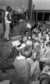 Popgala i Kumla,  24 augusti 1965

Två polismän sitter på huk och pratar med medlemmar ur publiken som står nedanför scenen. Ett piano i bakgrunden på scenen.