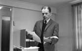 Diabetiker, 155 Ogestad, Fick Guldur 5 februari 1966

En man i rutig kavaj, svart väst, svart slips och vit skjorta håller i två pappersark. Han står inne på ett kontor.