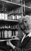 Sprithamstringen slut, 8 februari 1966

En kvinna som arbetar på Systembolaget klistrar upp en liten etikett med nummer och pris på whiskyflaskor som står på en hylla. Andra flaskor står på hyllor runtomkring. Kvinnan är klädd i arbetskläder.
