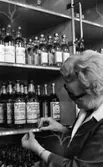 Sprithamstringen slut, 8 februari 1966

En kvinna som arbetar på Systembolaget klistrar upp en liten etikett med nummer och pris på whiskyflaskor som står på en hylla. Andra flaskor står på hyllor runtomkring. Kvinnan är klädd i arbetskläder.