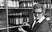 Sprithamstringen slut, 8 februari 1966

En kvinna som arbetar på Systembolaget klistrar upp en liten etikett med nummer och pris på whiskyflaskor som står på en hylla. Andra flaskor står på hyllor runtomkring. Kvinnan är klädd i arbetskläder.