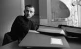 Student bostäder 1 februari 1966

En närbild på en student som sitter vid sitt skrivbord i sin studentlägenhet. På skrivbordet ligger fyra pärmar. I bakgrunden skymtar köket med diskbänk, kylskåp och lådor. En bordslampa syns till höger.