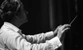 Cellibedache 13 juni 1966

En dirigent klädd i vit skjorta viftar med taktpinnen framför en orkester.