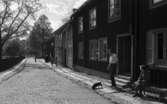 Wadköping, 28 maj 1966

Vy över Wadköping. En man med en tax kommer ut ur ett hus. En äldre kvinna sitter på en bänk invid huset. Enliten pojke kommer cyklande på gatan. Fler personer syns i bakgrunden av bilden.
