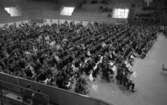 Blåsarträffen 28 maj 1966

En skor skara blåsinstrumentsmusiker sitter samlade i en stor sal. Publik sitter på läktare i bakgrunden.