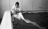 Loka brunn 22 juli 1966

En äldre man badar i bassängen och sparkar med benen på kurorten Loka brunn. Invid honom vid bassängkanten står en kvinna i vit arbetsrock och övervakar hans träning.