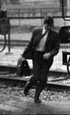 På stationen 1 16 augusti 1966

En herre klädd i kostym, skjorta och slips springer över järnvägsspåren på Örebro station i strilande regn.