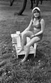 Mosåsflicka, Brandkårsuppvisning, Harar, Transportkillar 27 maj 1967

En flicka klädd i rutig bikini och vit hatt sitter på en stol utomhus i gröngräset.
