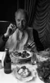 Kräftor 9 augusti 1967

En man med vit servett över hela bröstet sitter och äter kräftor vid ett bord med vit duk på. Han har ett fat framför sig med kräftor på, ett ölglas samt ett snapsglas. Även en flaska öl står på bordet. Ett litet fat med smör står i förgrunden.