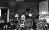 Kräftor- Karlslundsgård 5 aug. 1967

En äldre herre sitter i en fåtölj och håller i en käpp. Han är klädd i rutig skjorta och rutig kavaj. Bakom honom syns bord, stolar, en soffa, en kakelugn i högra hörnet samt en bonad på väggen. En till fåtölj står till höger om den äldre mannen.