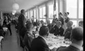 Kungen I3 28 augusti 1967

Kung Gustav VI Adolf besöker Örebro Livregementes Grenadjärer i Grenadjärsstaden. Han sitter vid ett dukat bord en matsal på regementet tillsammans med militärer och andra personer. På bordet står statyetter föreställande soldater i miniatyr på ömse sidor om mattallriken. Bakom kungen står en militär med befälsbricka om halsen samt en fana i handen. På ömse sidor om militären står kvinnor klädda i arbetsuniformer och förkläden. En man som suttit mittemot kungen under måltiden har rest sig upp och håller tal till kungen. En fotograf med kamera i handen syns till vänster.