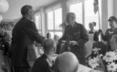 Kungen I3 28 augusti 1967

Kung Gustav VI Adolf besöker Örebro Livregementes Grenadjärer i Grenadjärsstaden. Han sitter vid ett dukat bord en matsal på regementet tillsammans med militärer och andra personer. På bordet står statyetter föreställande soldater i miniatyr på ömse sidor om mattallriken. Bakom kungen står en militär med befälsbricka om halsen samt en fana i handen. På ömse sidor om militären står kvinnor klädda i arbetsuniformer och förkläden. En man står upp mittemot kungen och skakar dennes hand. Kungen håller en bok i sin vänstra hand.