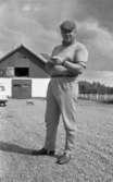 Orubricerad 5 augusti 1967 Travkusk Bengt Nilsson

Travkusken Bengt Nilsson står på en gårdsplan med ett block i sina händer. Han är klädd i rutig keps, ljus tröja och ljusa byxor samt skor. I bakgrunden syns en katt som går över gårdsplanen, en bil samt ett hus.