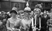 Orubricerad 21 augusti 1967

Tre kvinnor står på en gårdsplan i Wadköping. Kvinnan till vänster är klädd i blommig klänning och hatt, kvinnan i mitten är klädd i en lustig hatt och vit kappa och bär glasögon. Kvinnan till höger är klädd i mörka 1800-talskläder: en mörk klänning, mörk krage, mörk hatt och vita halvvantar. Hon håller i en vit ljusstake. Bakom de tre kvinnorna står en publik och tittar på.