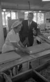 Orubricerad 21 augusti 1967

Direktören står vid en kvinna som jobbar på Örebro Kexfabrik. Han är klädd i mörk kavaj, mörka byxor, vit skjorta och mörk slips. Han håller ett kex i sin vänstra hand. Kvinnan är klädd i vita arbetskläder och har en vit mössa på huvudet. Hon är i färd med att dela stora fyrkantiga kexbitar i små delar.