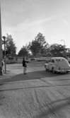 Knuttarna har bil 24 juli 1967

En långhårig, ung man står och liftar på gatan nära en järnvägsövergång. Bilar kör förbi. Han är klädd i mörk jacka,   ljusa byxor och mörka skor.